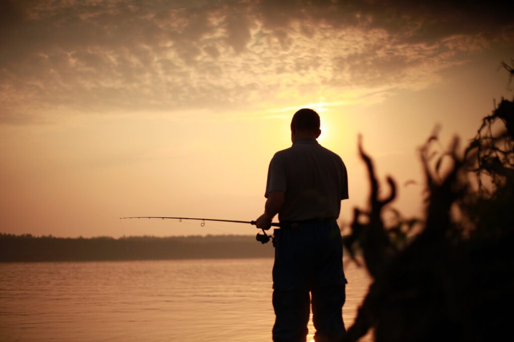 A man at sunset is fishing and fishing on the river with a fishing rod.